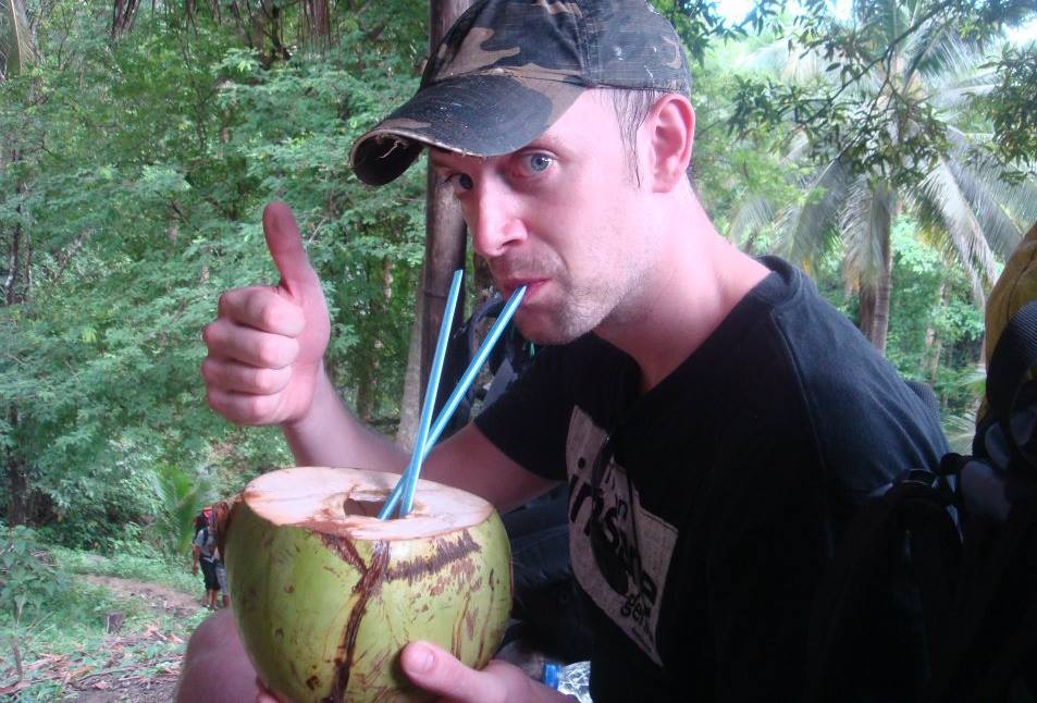 Dan up a mountain in the jungle drinking from a coconut